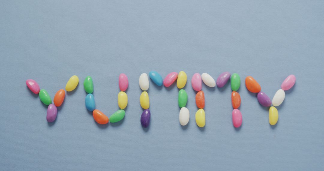 Colorful Jelly Beans Arranged to Spell 'YUMMY' on Blue Background - Free Images, Stock Photos and Pictures on Pikwizard.com