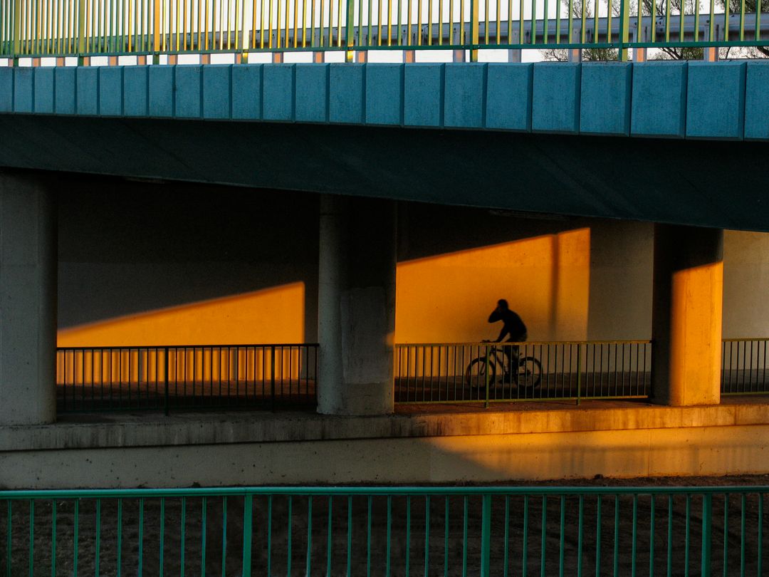 Cyclist under modern urban bridge during sunset - Free Images, Stock Photos and Pictures on Pikwizard.com