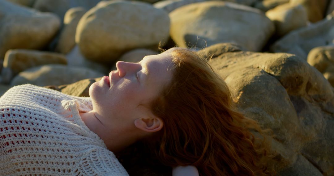 Young Caucasian woman relaxes on a rocky beach at sunset - Free Images, Stock Photos and Pictures on Pikwizard.com