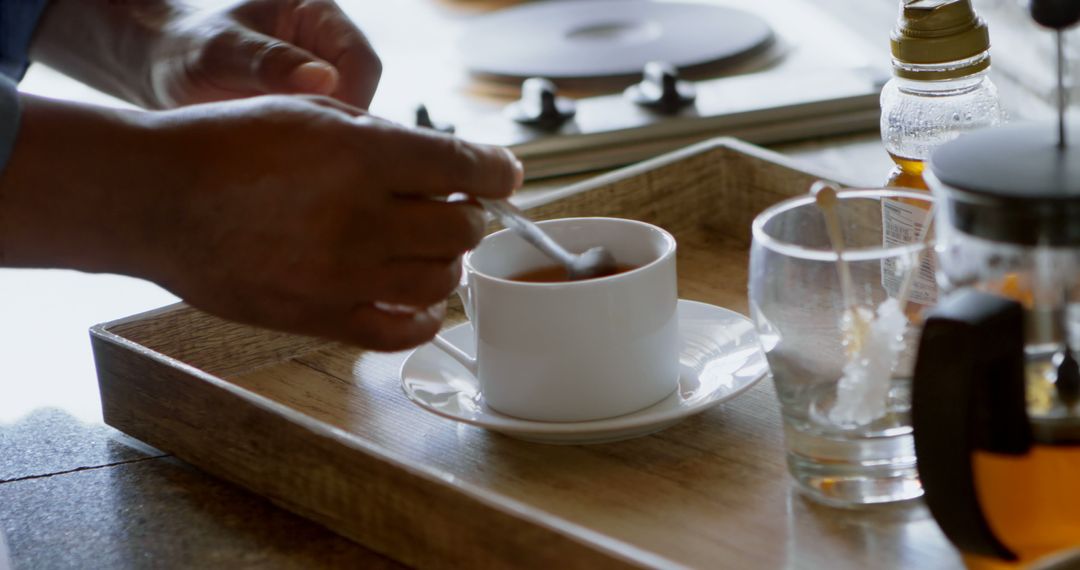 Person Stirring Tea in Cup on Wooden Tray in Rustic Kitchen - Free Images, Stock Photos and Pictures on Pikwizard.com