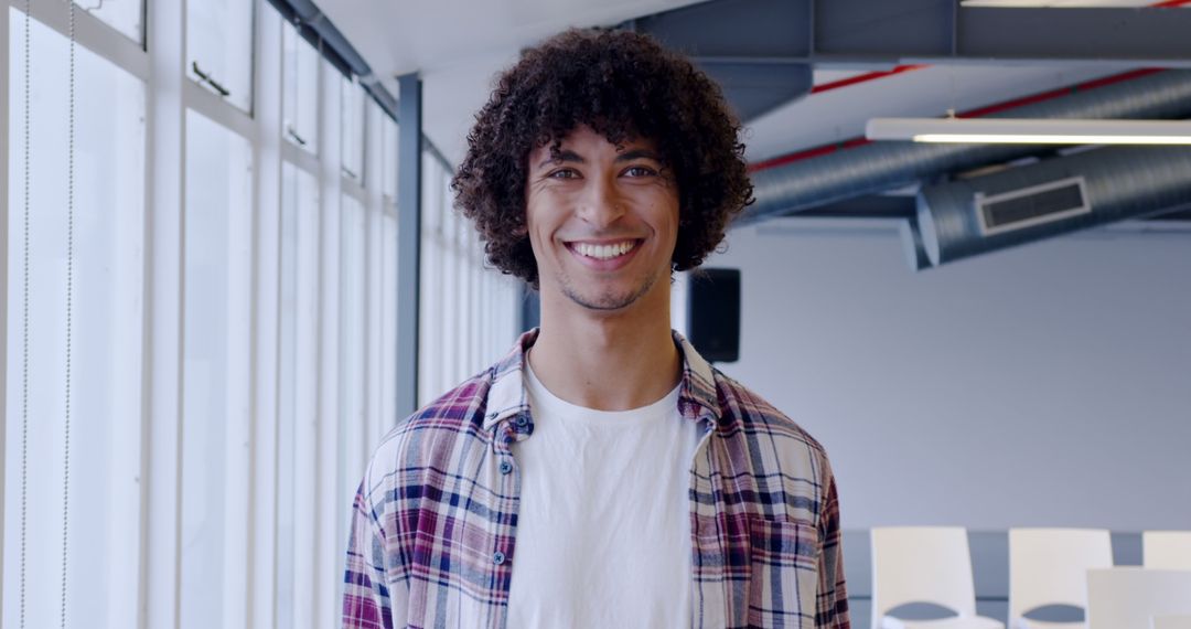 Smiling Young Man with Curly Hair in Modern Office Space - Free Images, Stock Photos and Pictures on Pikwizard.com