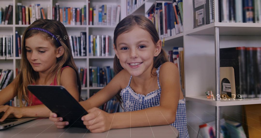 Girls collaborating with tablet and laptop in library smiling while learning technology