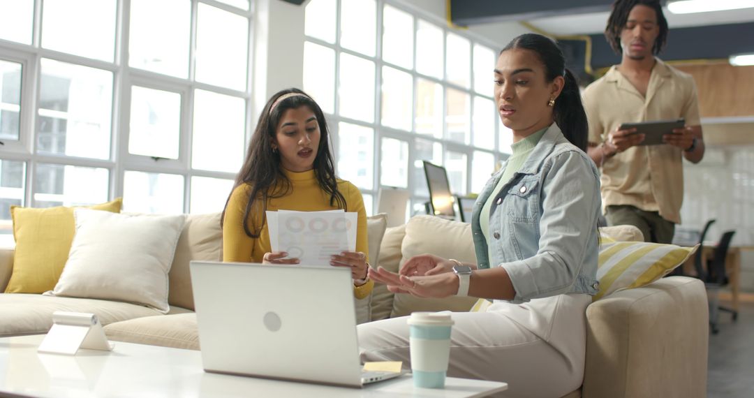 Diverse young professionals collaborating, brainstorming on couch in modern office lounge