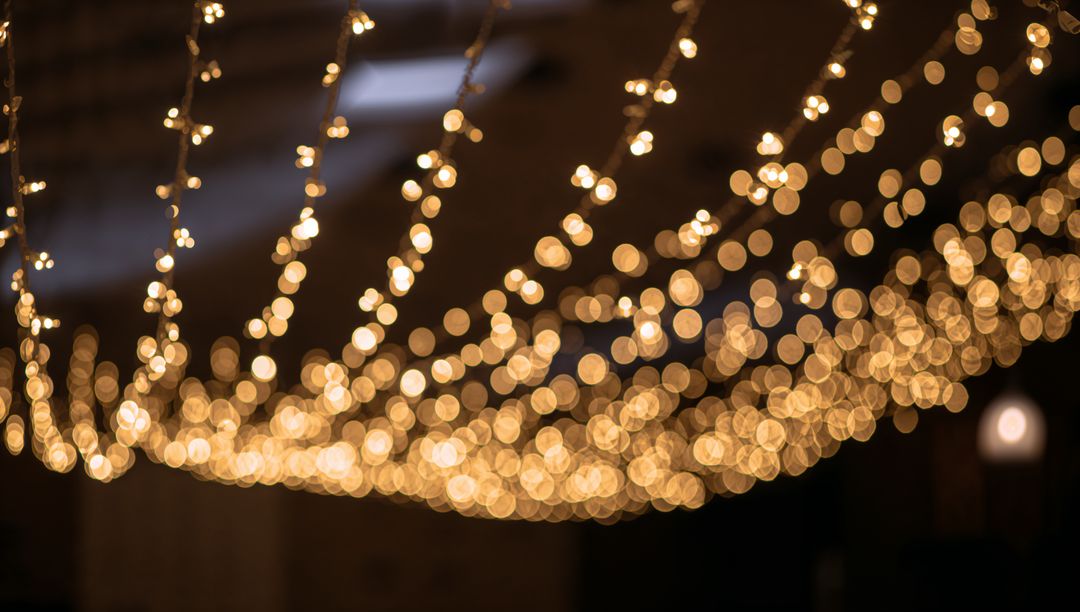Warm bokeh canopy of hanging string lights over rustic interior venue rafters