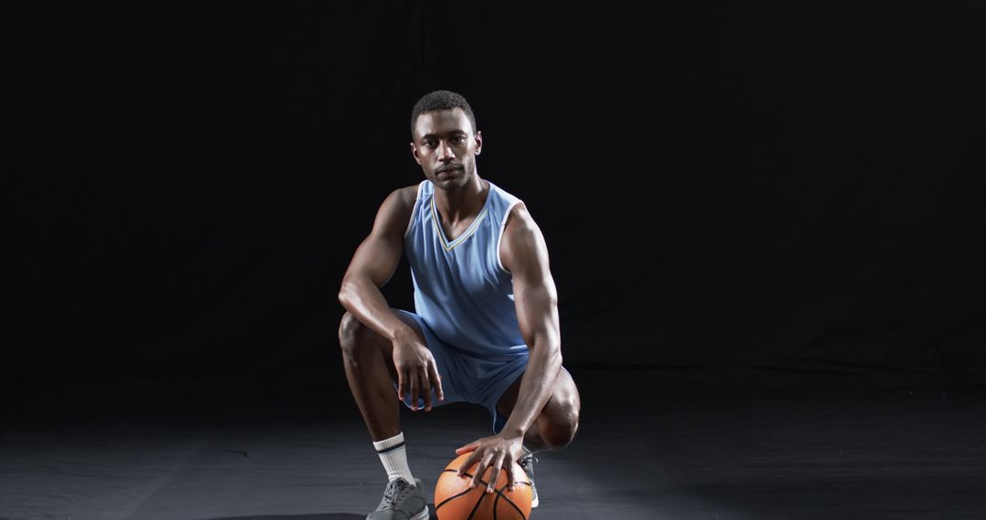 Athlete Crouching with Basketball in Blue Uniform on Dark Background