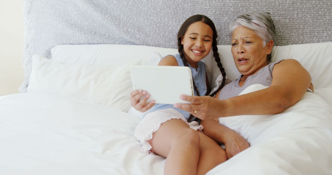 Grandmother and Granddaughter Relaxing on Bed with Tablet - Free Images, Stock Photos and Pictures on Pikwizard.com