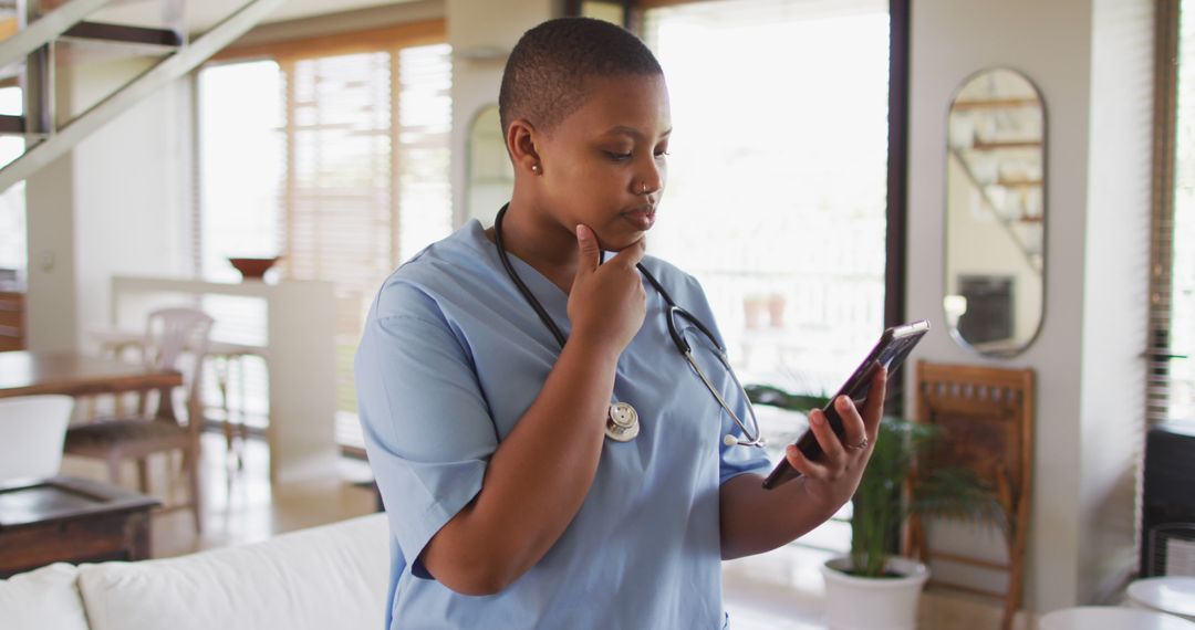 Nurse in blue scrubs looking at tablet at home, thoughtful expression - Free Images, Stock Photos and Pictures on Pikwizard.com