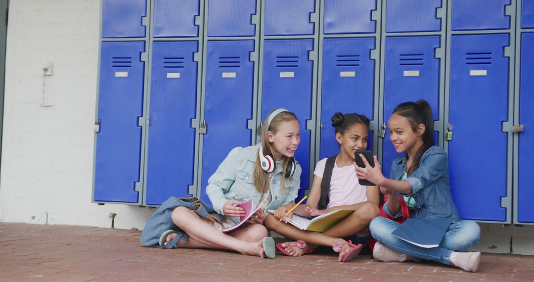 Happy Students Sitting by Lockers Sharing Phone - Free Images, Stock Photos and Pictures on Pikwizard.com