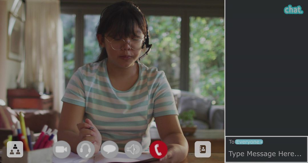 Chinese student studying at home during video lesson wearing headset and taking notes