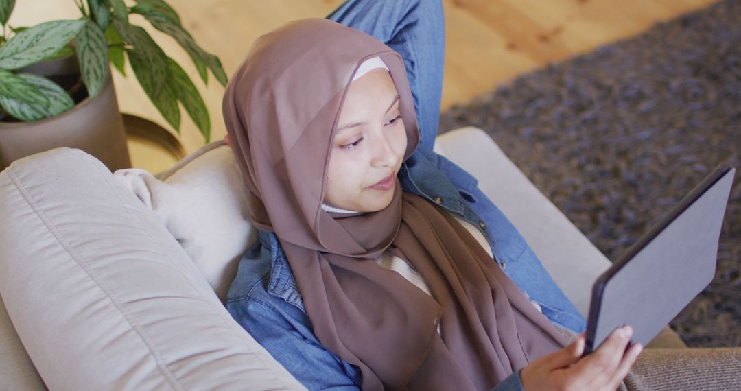 Muslim Woman Relaxing at Home Using Digital Tablet, Leisure Technology Concept - Free Images, Stock Photos and Pictures on Pikwizard.com