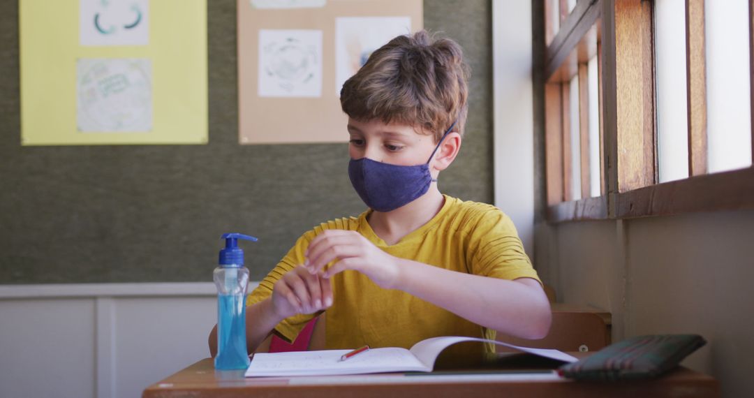 Young Boy Sanitizing Hands while Wearing Facemask in Classroom