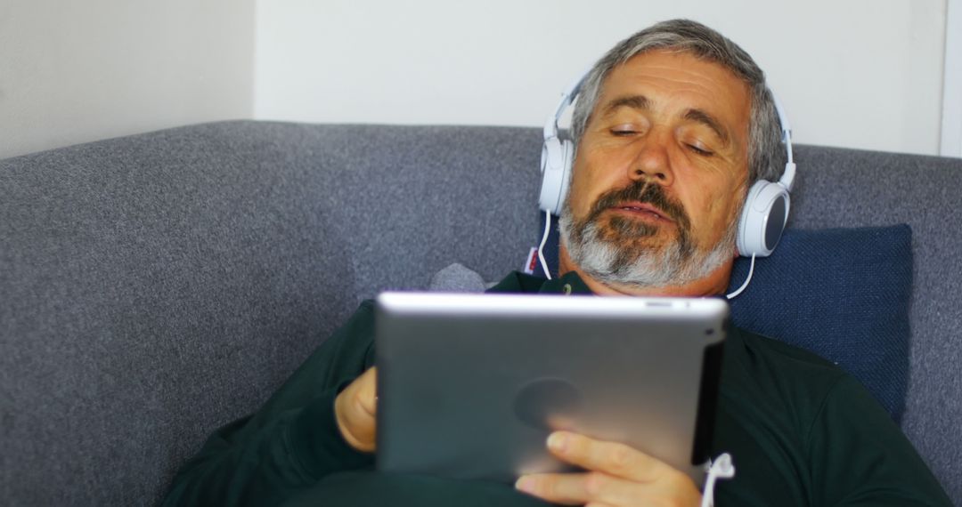 Senior Man Relaxing on Sofa Using Tablet and Wearing Headphones - Free Images, Stock Photos and Pictures on Pikwizard.com