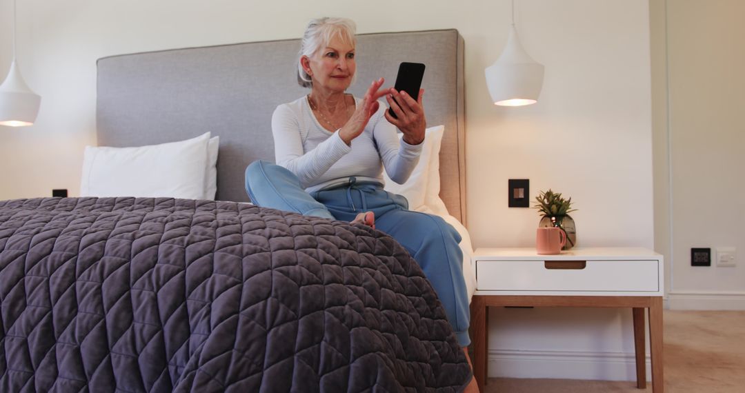 Senior Woman Using Smartphone while Sitting on Modern Bed at Home