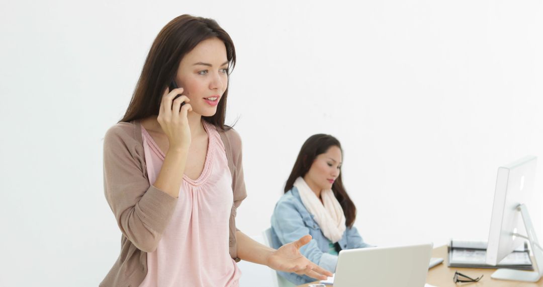 Young Woman Talking on Phone While Colleague Working on Computer in Office - Free Images, Stock Photos and Pictures on Pikwizard.com