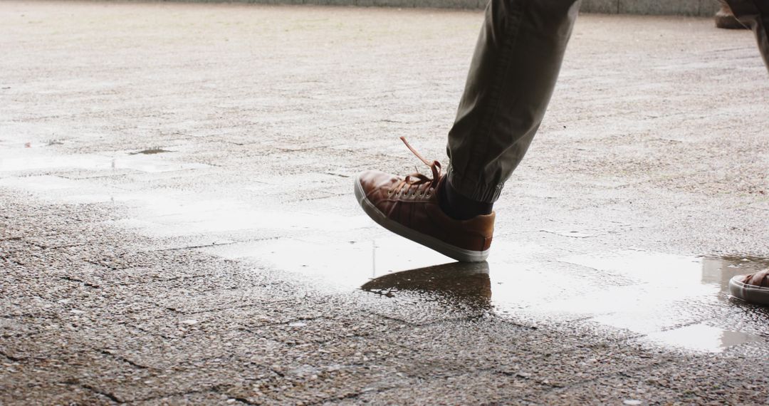 Mature man stepping through puddle on wet urban pavement with brown sneakers