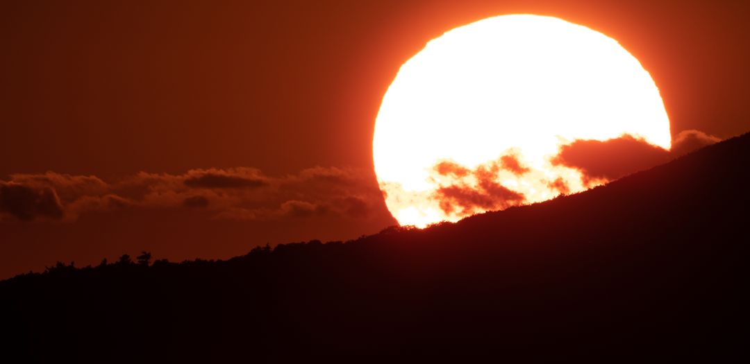 Massive Sunsetting Behind Mountain Silhouette with Fiery Red Sky and Cloud Detail