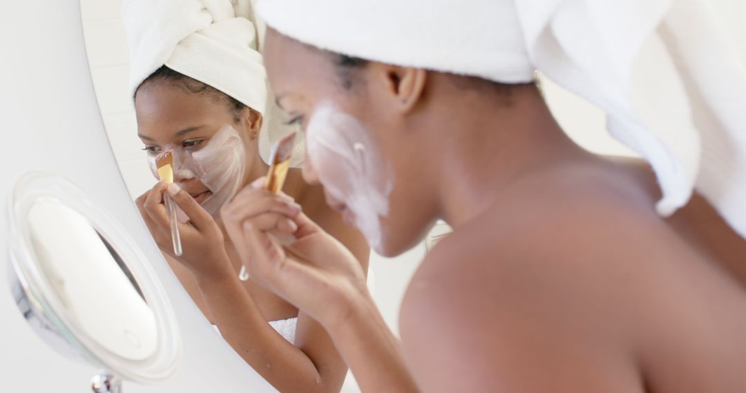 Woman Applying Facial Mask in Front of Mirror with Towel Wrapped Around Head - Free Images, Stock Photos and Pictures on Pikwizard.com