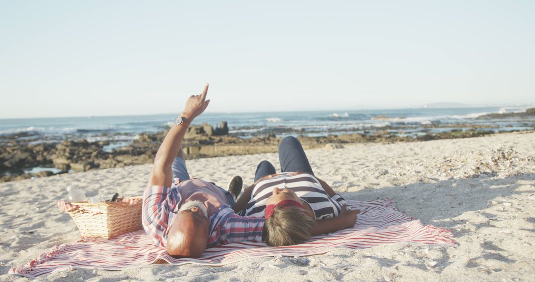 Senior Couple Relaxing on Beach Picnic Pointing Toward Horizon - Free Images, Stock Photos and Pictures on Pikwizard.com