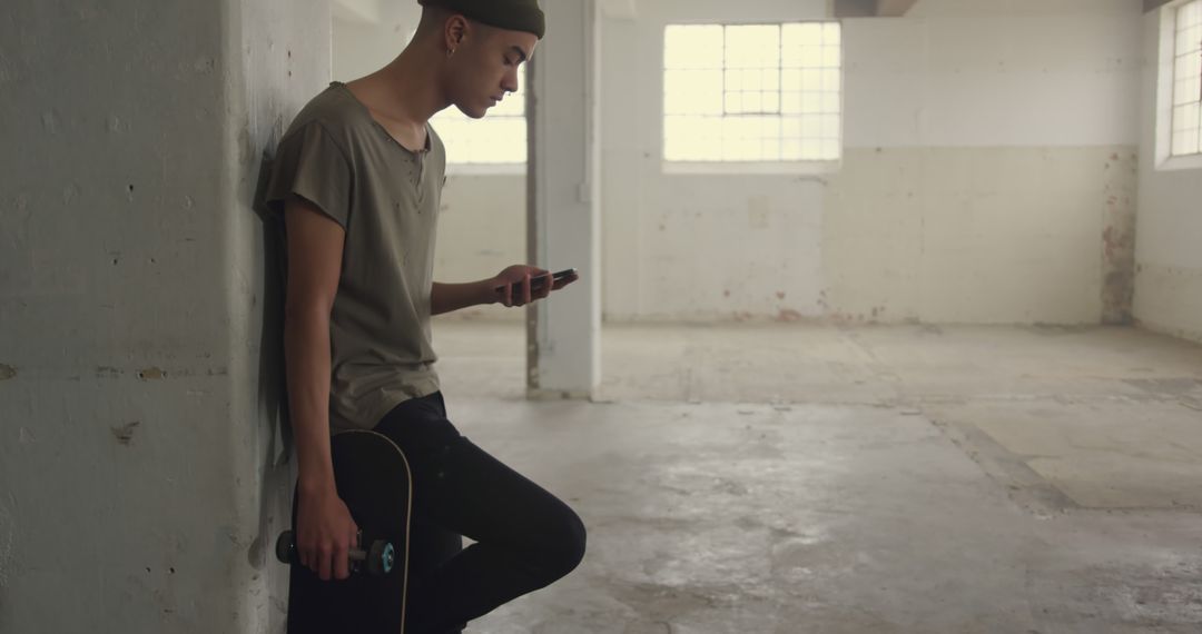 Young Hipster Skater Checking Smartphone in Empty Warehouse - Free Images, Stock Photos and Pictures on Pikwizard.com