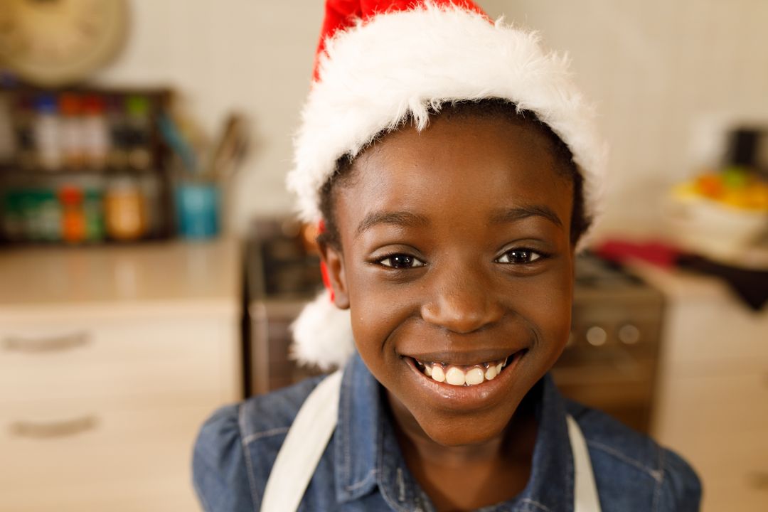 Smiling African-American Girl Wearing Santa Hat in Kitchen - Free Images, Stock Photos and Pictures on Pikwizard.com