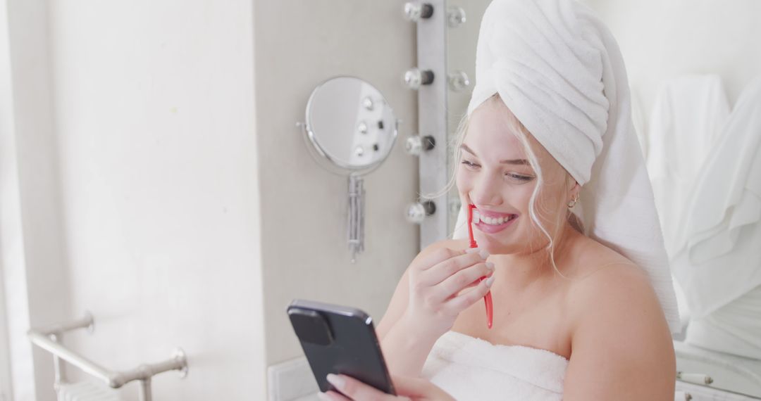 Smiling Woman in Towel and Hair Wrap Using Smartphone in Bathroom - Free Images, Stock Photos and Pictures on Pikwizard.com