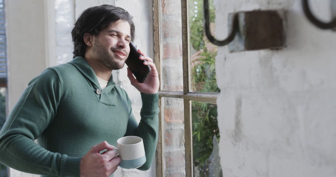 Smiling Man Talking on Phone and Drinking Coffee by Window - Free Images, Stock Photos and Pictures on Pikwizard.com