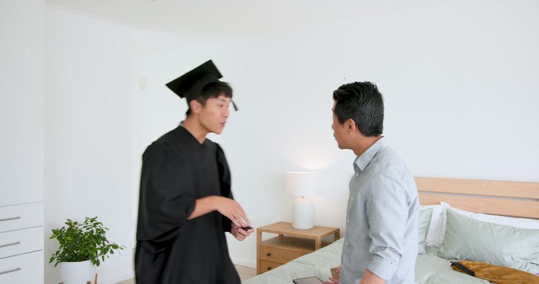 Father Congratulating Son Wearing Graduation Gown at Home