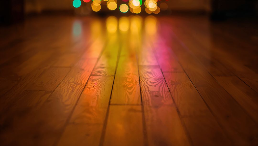 Warm hardwood floor reflecting colorful bokeh lights with visible wood grain and glow