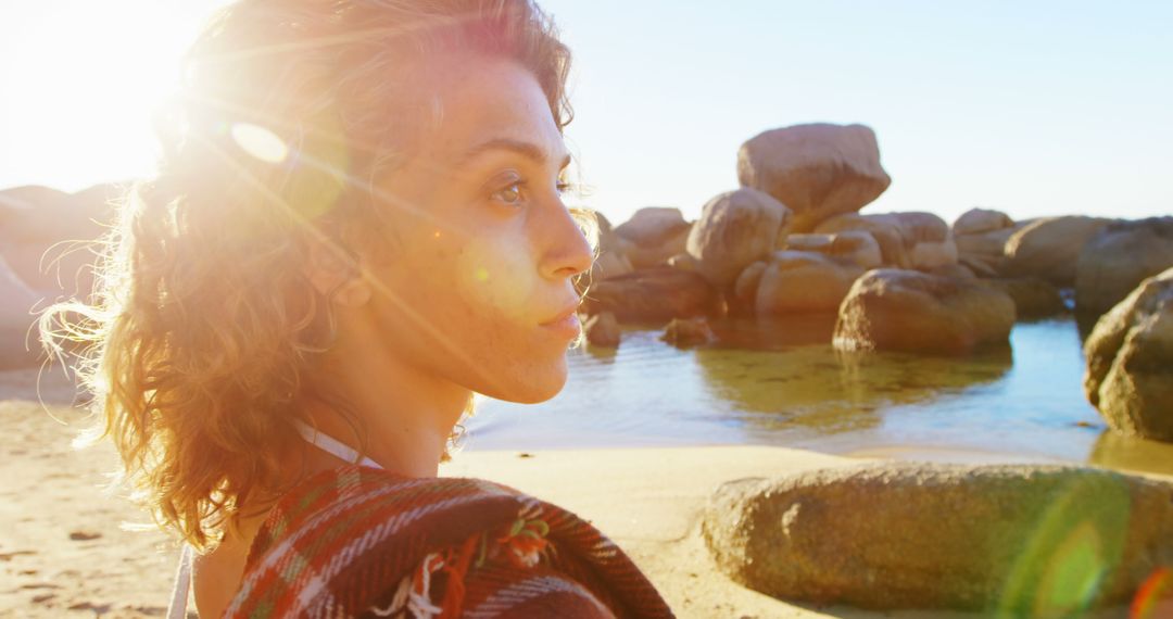 Sunlit Young Woman in Contemplation by Rocky Beach - Free Images, Stock Photos and Pictures on Pikwizard.com