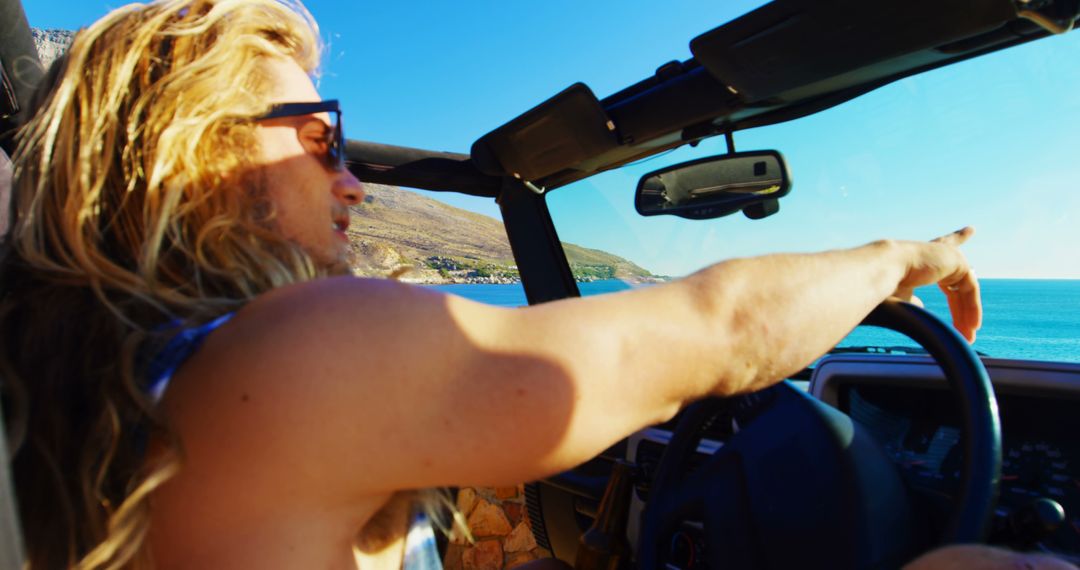 Young Man Driving Convertible by the Ocean Pointing in Distance - Free Images, Stock Photos and Pictures on Pikwizard.com