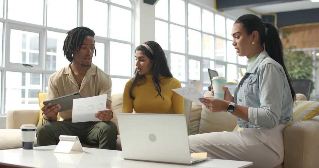 Multicultural team reviewing charts and tablet in modern office lounge