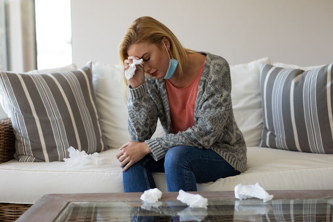 Woman with a cold sits on couch surrounded by used tissues. - Free Images, Stock Photos and Pictures on Pikwizard.com