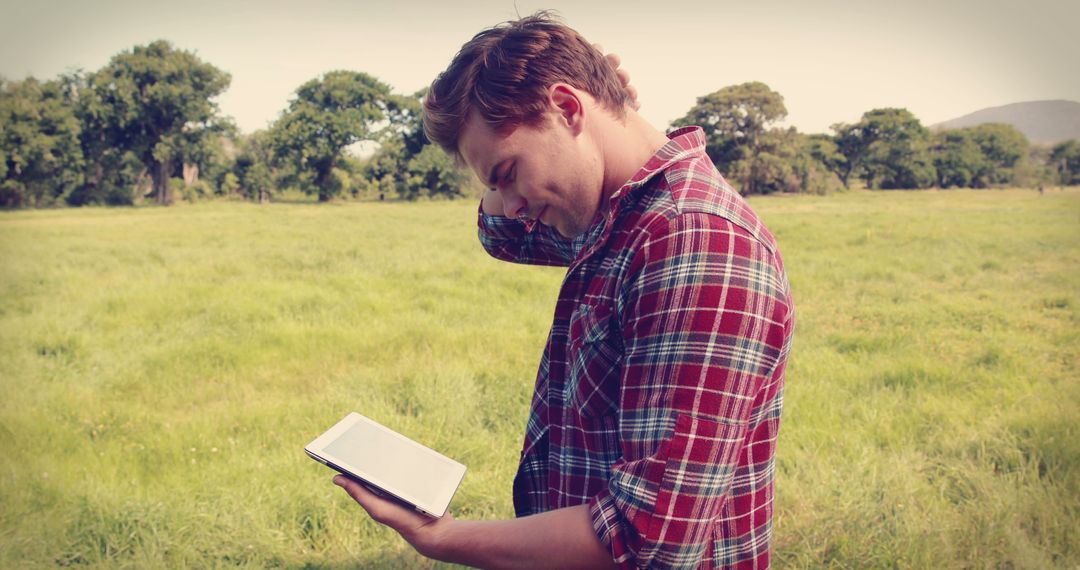 Young Man Reading Tablet Outdoors in Green Field - Free Images, Stock Photos and Pictures on Pikwizard.com