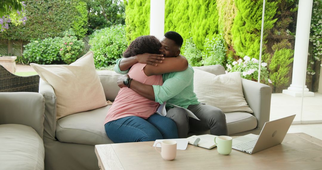 Couple Embracing on Comfortable Patio Setting with Laptop and Mugs