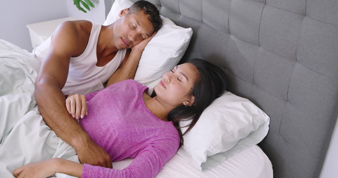 Couple sleeping peacefully in modern bed cuddling under white sheets with cozy headboard