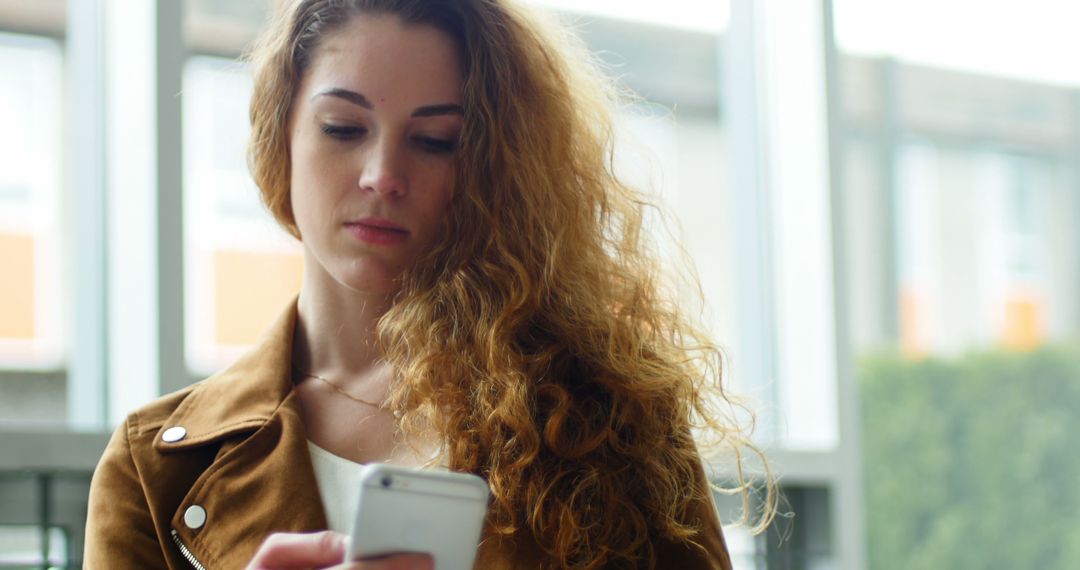 Young Woman with Curly Hair Using Smartphone in Modern Setting - Free Images, Stock Photos and Pictures on Pikwizard.com