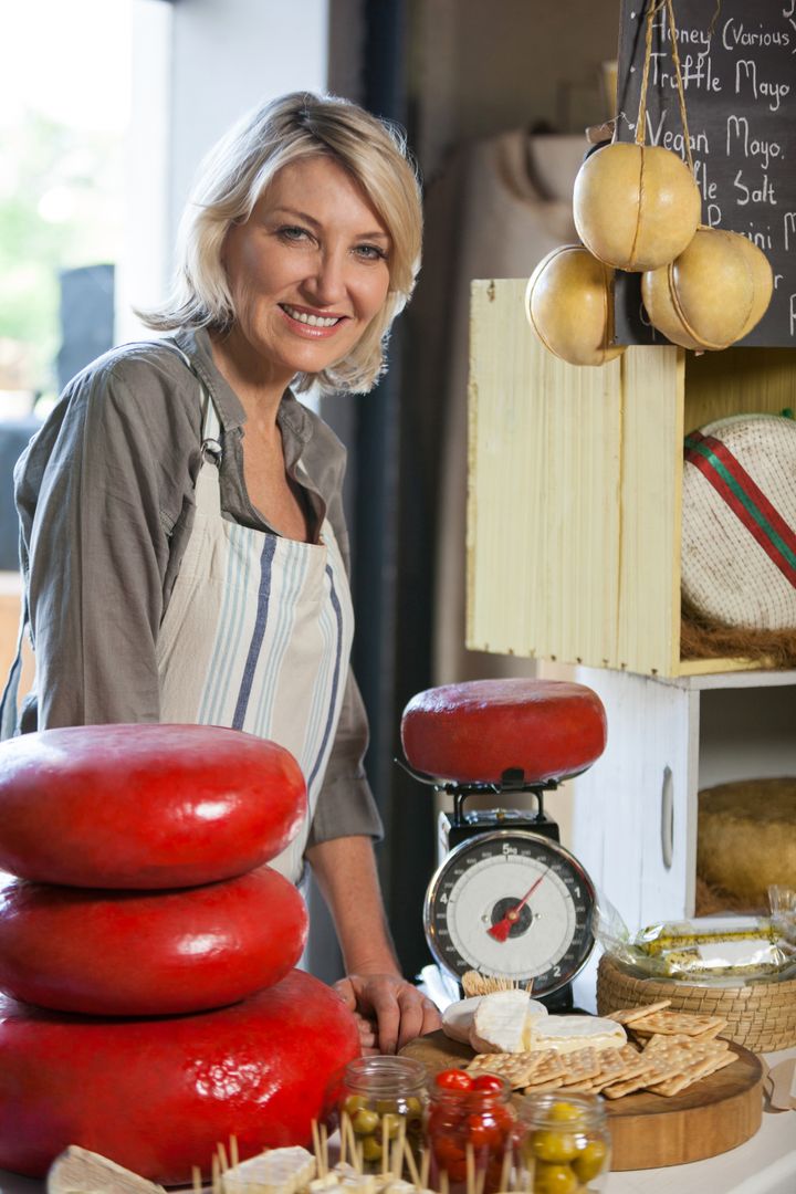 Smiling Senior Cheesemonger with Wheels of Gourmet Cheese