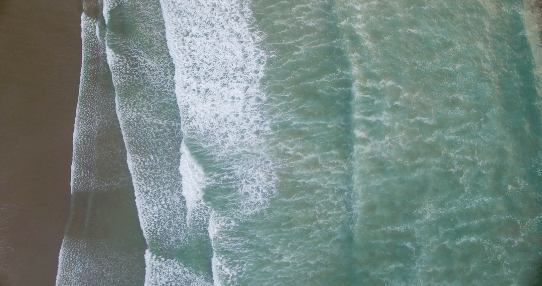 Transparent Waves Crashing on Sandy Beach from Aerial Perspective