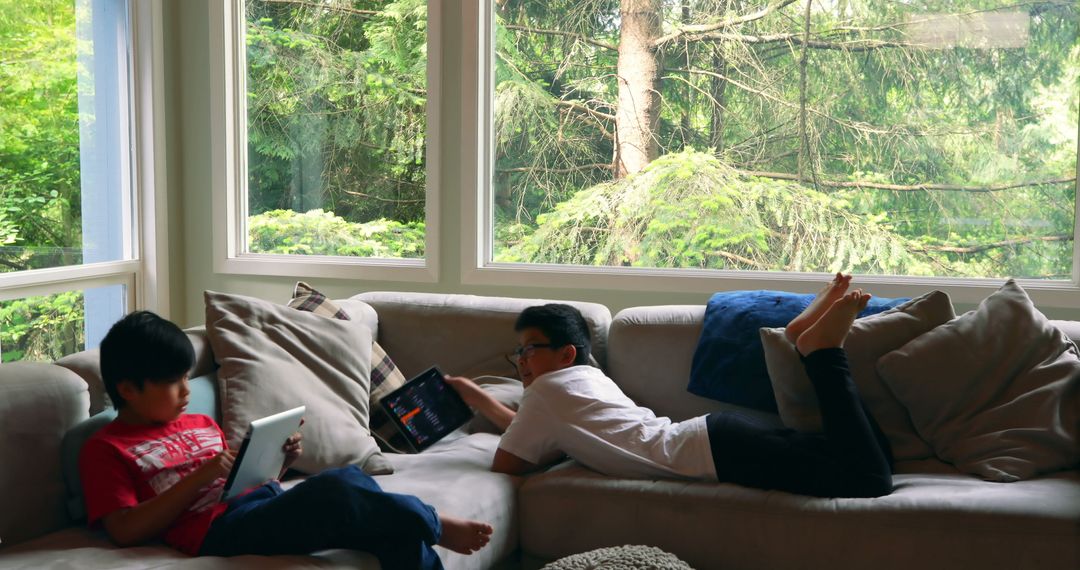 Children Relaxing on Sofa Using Digital Tablets Near Large Windows - Free Images, Stock Photos and Pictures on Pikwizard.com