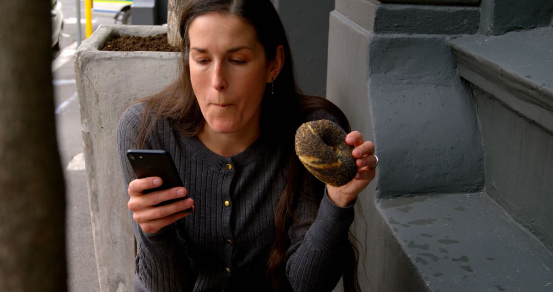 Woman with Donut Checking Smartphone Outdoors - Free Images, Stock Photos and Pictures on Pikwizard.com