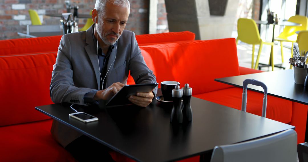 Mature Businessman Working on Tablet in Modern Cafe - Free Images, Stock Photos and Pictures on Pikwizard.com