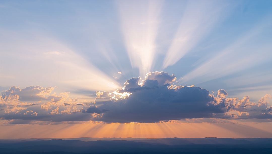 Sun rays bursting from cumulus cloud during sunrise over distant ridges