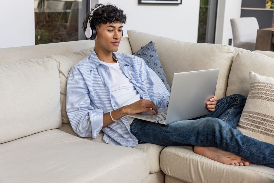 Man Relaxing on Sofa Using Laptop with Headphones