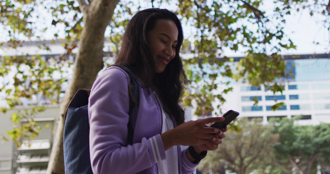 Asian woman smiling while using smartphone standing in the park - Free Images, Stock Photos and Pictures on Pikwizard.com