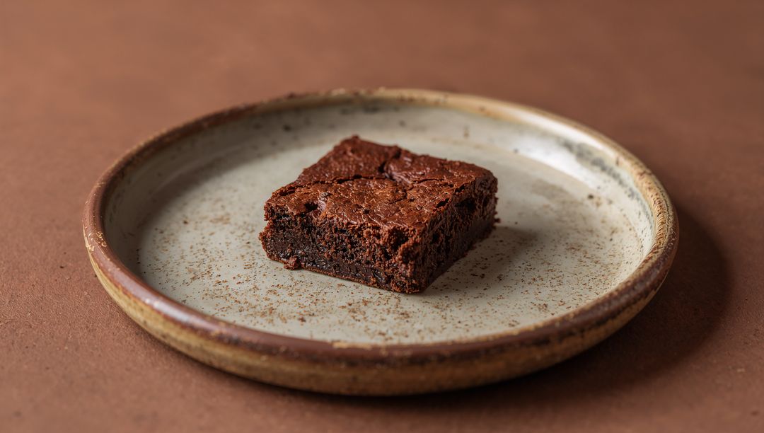Chocolate Brownie Square on Rustic Speckled Plate with Cocoa Crumbs Minimalist Food