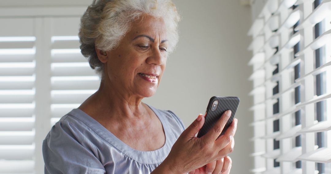 African american senior woman using smartphone and looking out of the window at home - Free Images, Stock Photos and Pictures on Pikwizard.com