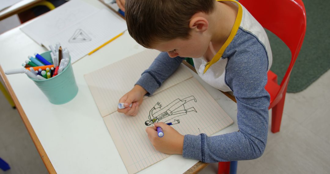 Young Schoolboy Drawing in Classroom on Notepad