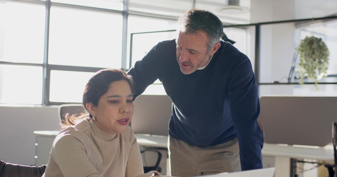 Senior mentor guiding diverse coworker reviewing documents on laptop in bright office