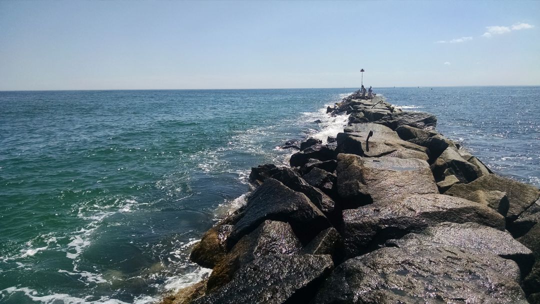 Rocky Pier Extending Into Ocean With Fisherman