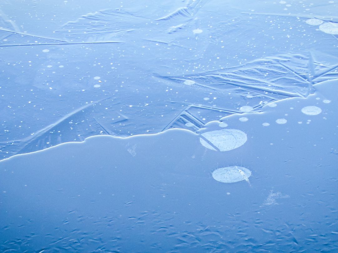 Blue Frozen Lake Surface with Air Bubbles and Fractured Ice Texture Abstract Winter